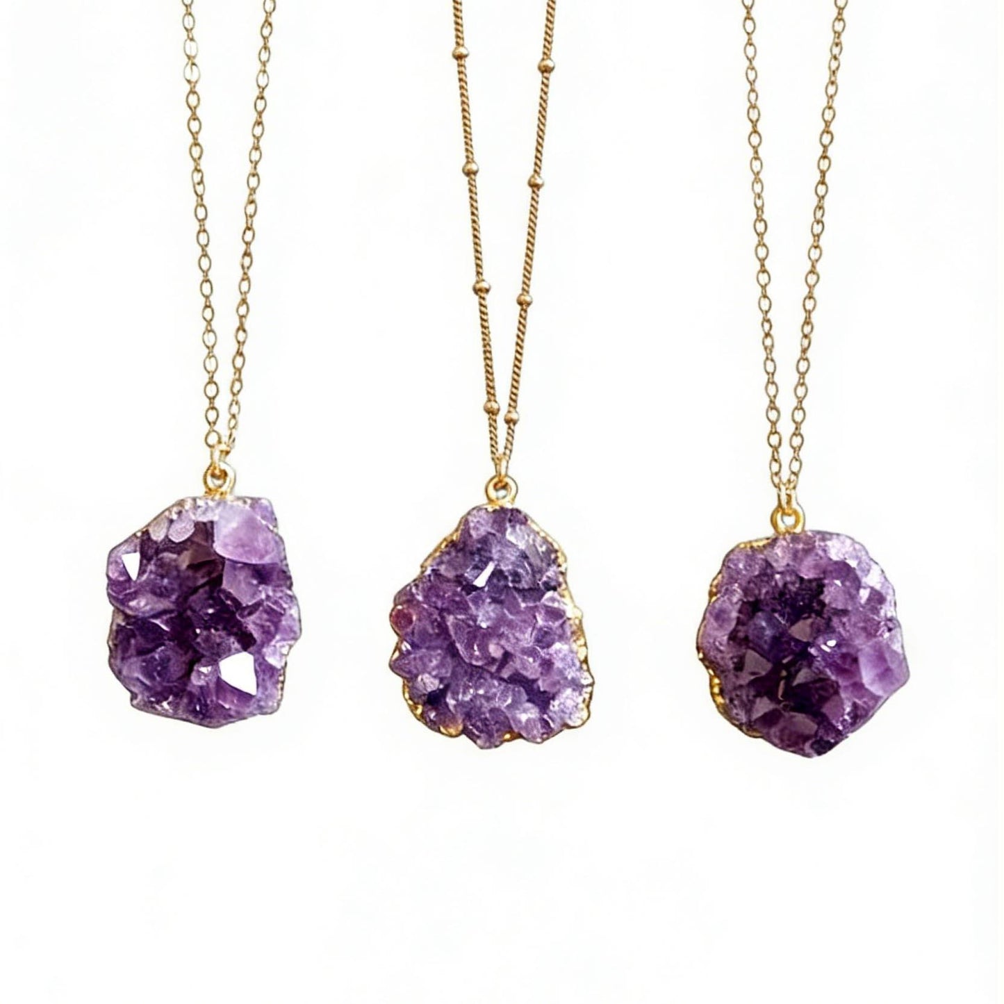 Three purple amethyst pendant necklaces on gold chains against a white background