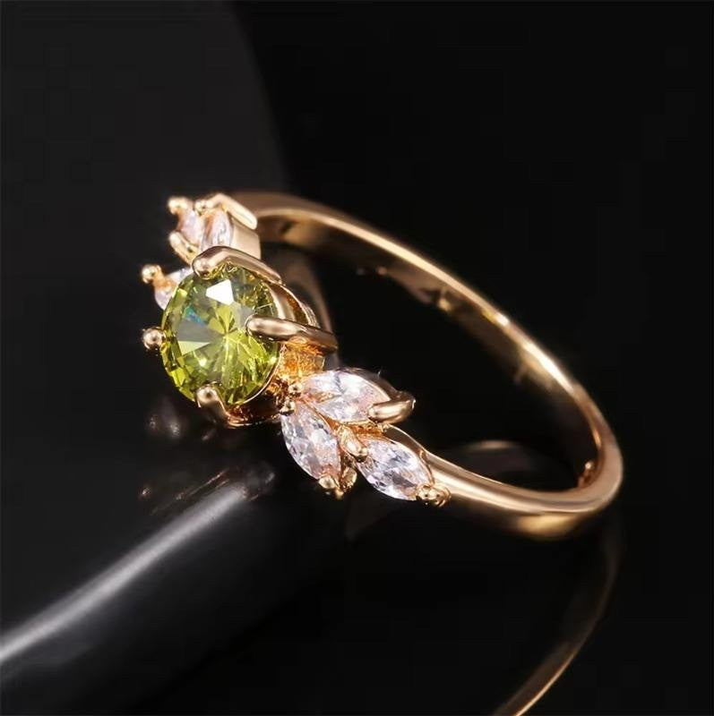 Gold ring with a green gemstone and smaller clear stones on a dark background