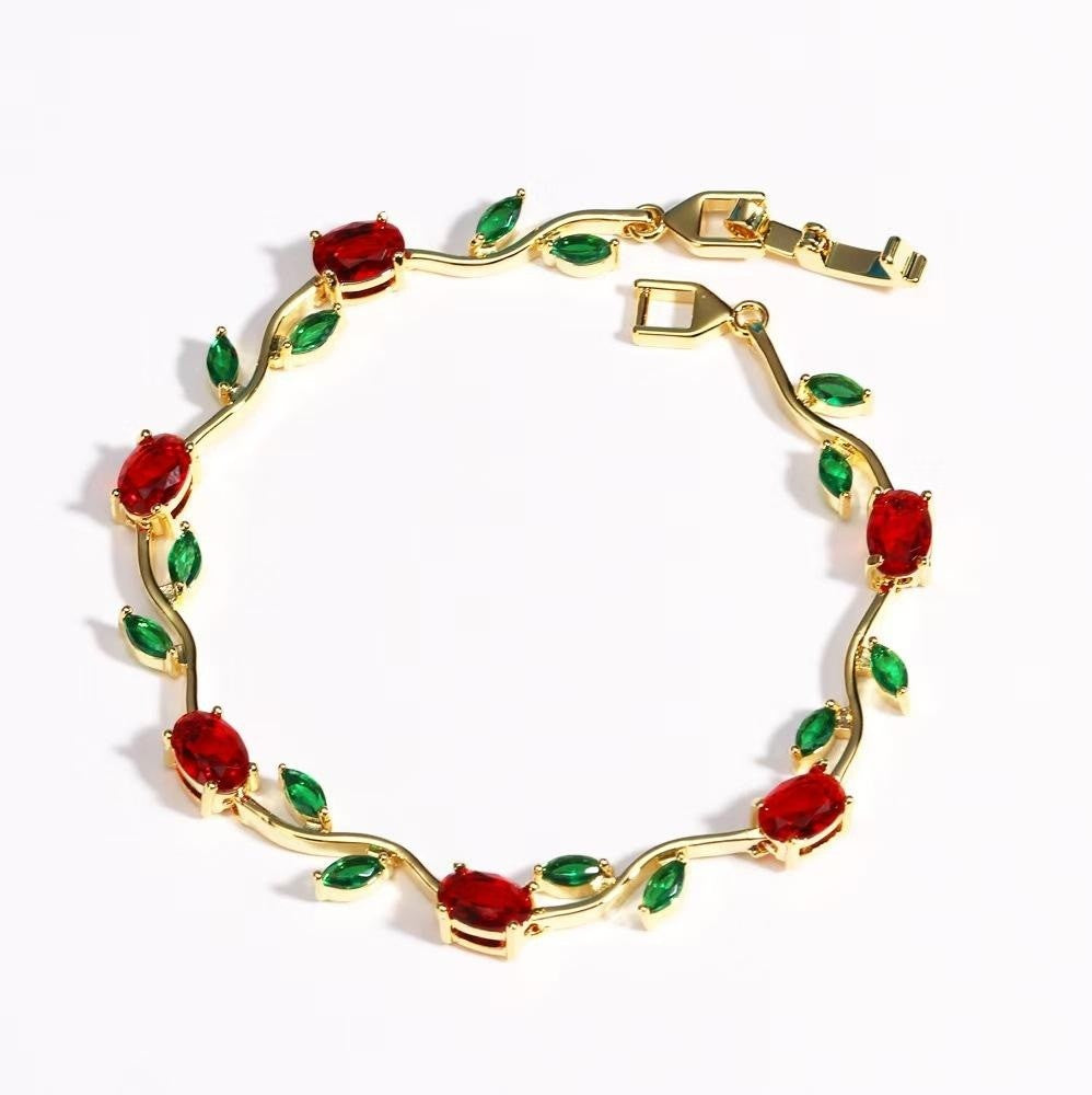 Gold bracelet with red and green gemstones on a white background