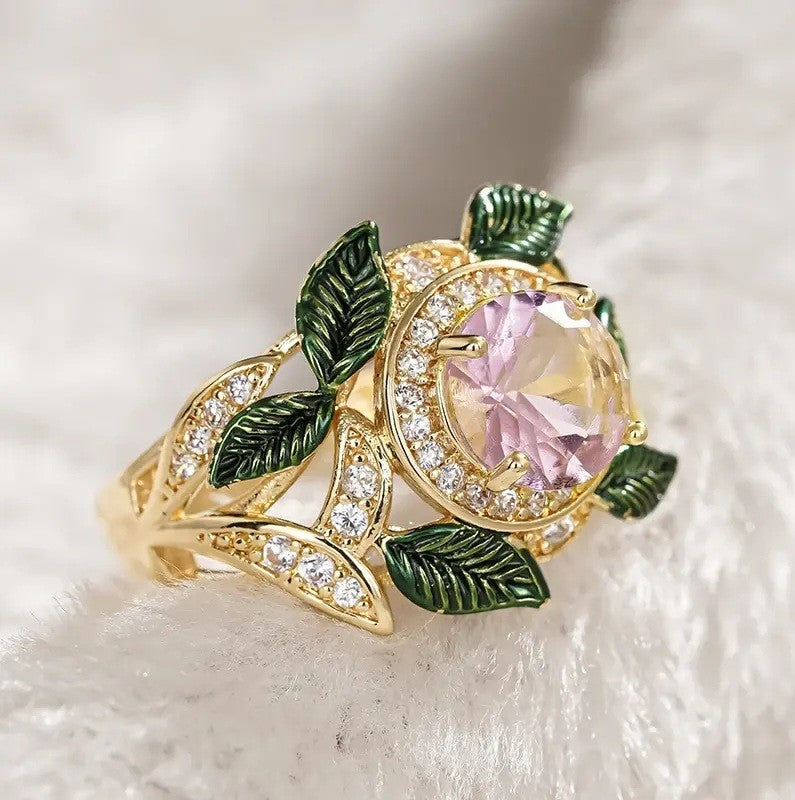 Gold ring with pink gemstone and green leaves on a white background