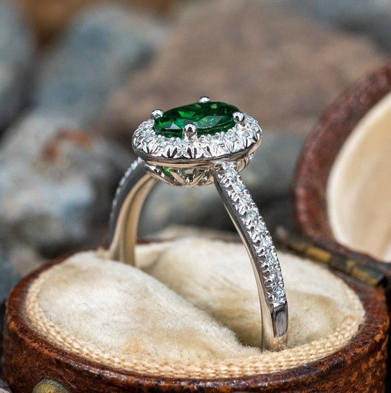 Silver ring with a green gemstone in a wooden box with a stone background