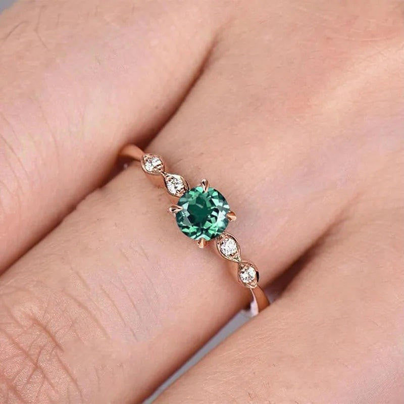 Rose gold ring with a green gemstone on a finger