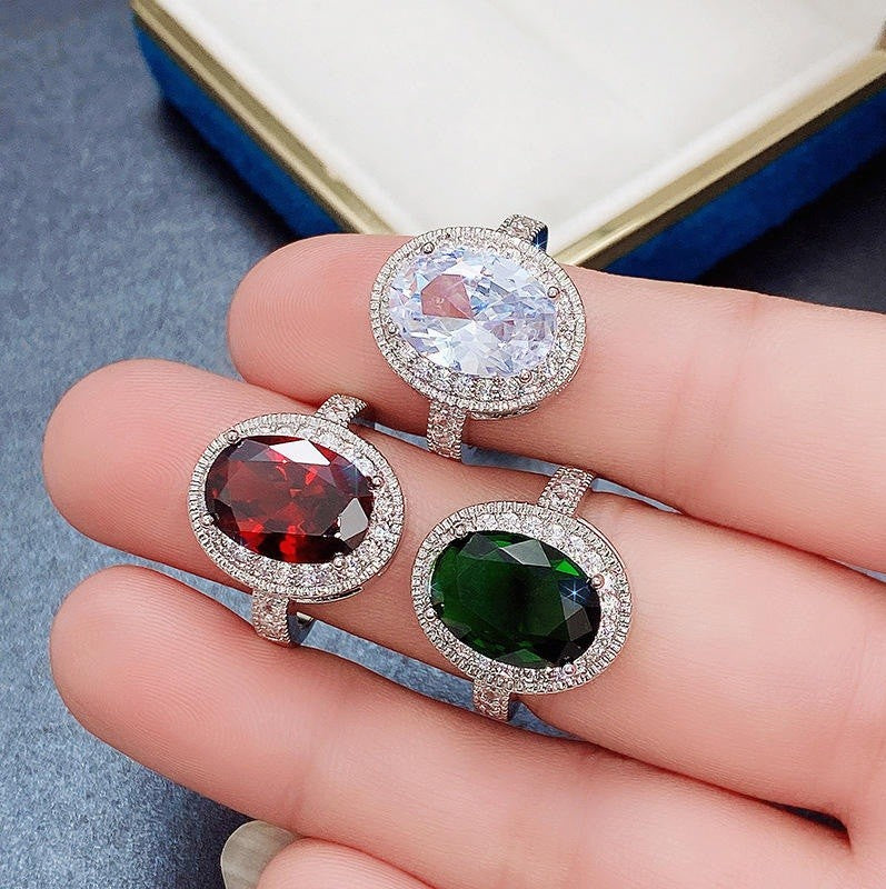 Three gemstone rings with different colored stones held on a hand against a blurred background.