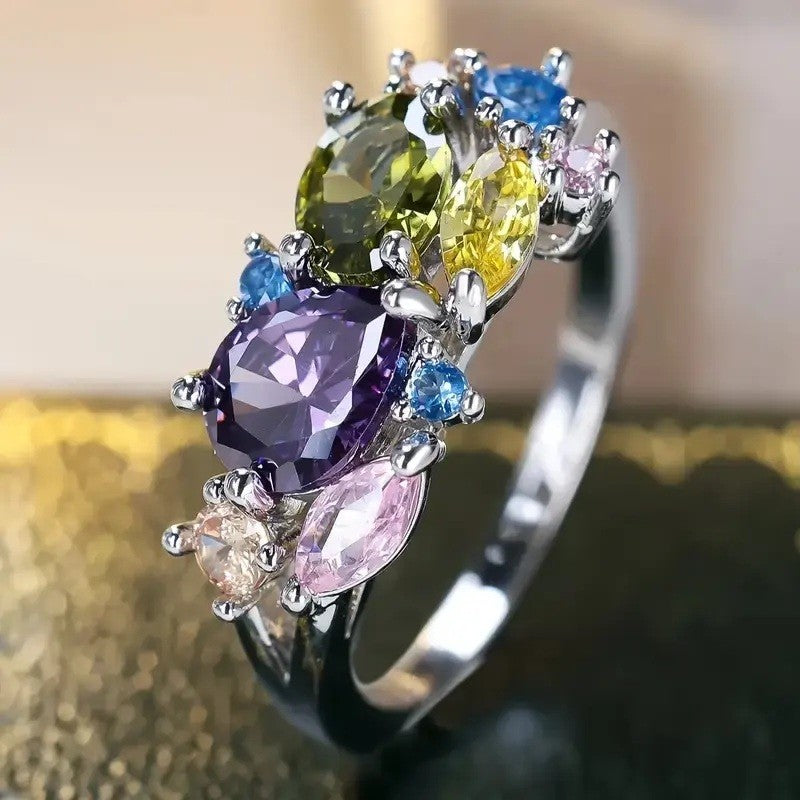 Multicolored gemstone ring with a silver band on a reflective surface.