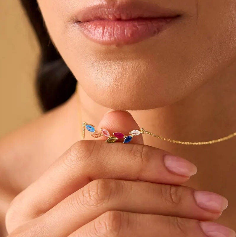 Close-up of a person wearing a gold necklace with colorful gemstones.