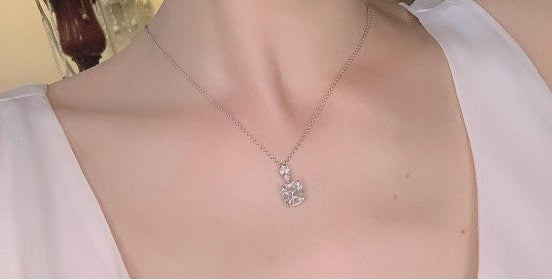 A delicate silver-toned chain necklace with a small clear crystal pendant, shown worn on a model's neck over a white top.