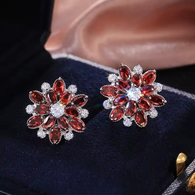 Pair of floral earrings with red gemstones on a dark fabric background
