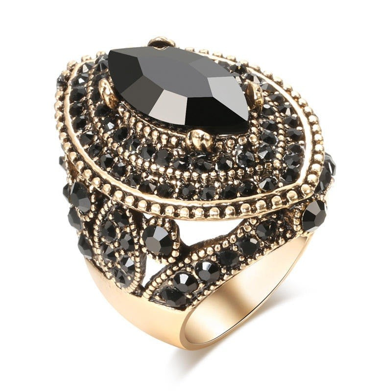 A gold-tone statement ring featuring a large marquise-cut black gemstone and multiple tiers of small round and faceted black stones, set against a plain white background.