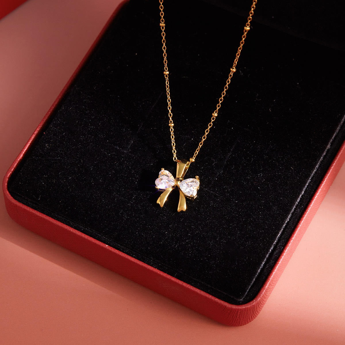 Gold necklace with a bow-shaped pendant on a black cushion inside a red box.