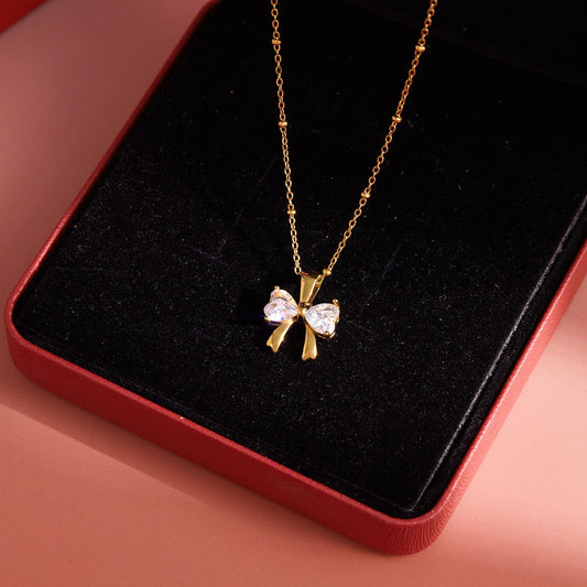 Gold necklace with a bow-shaped pendant on a black cushion inside a red box.