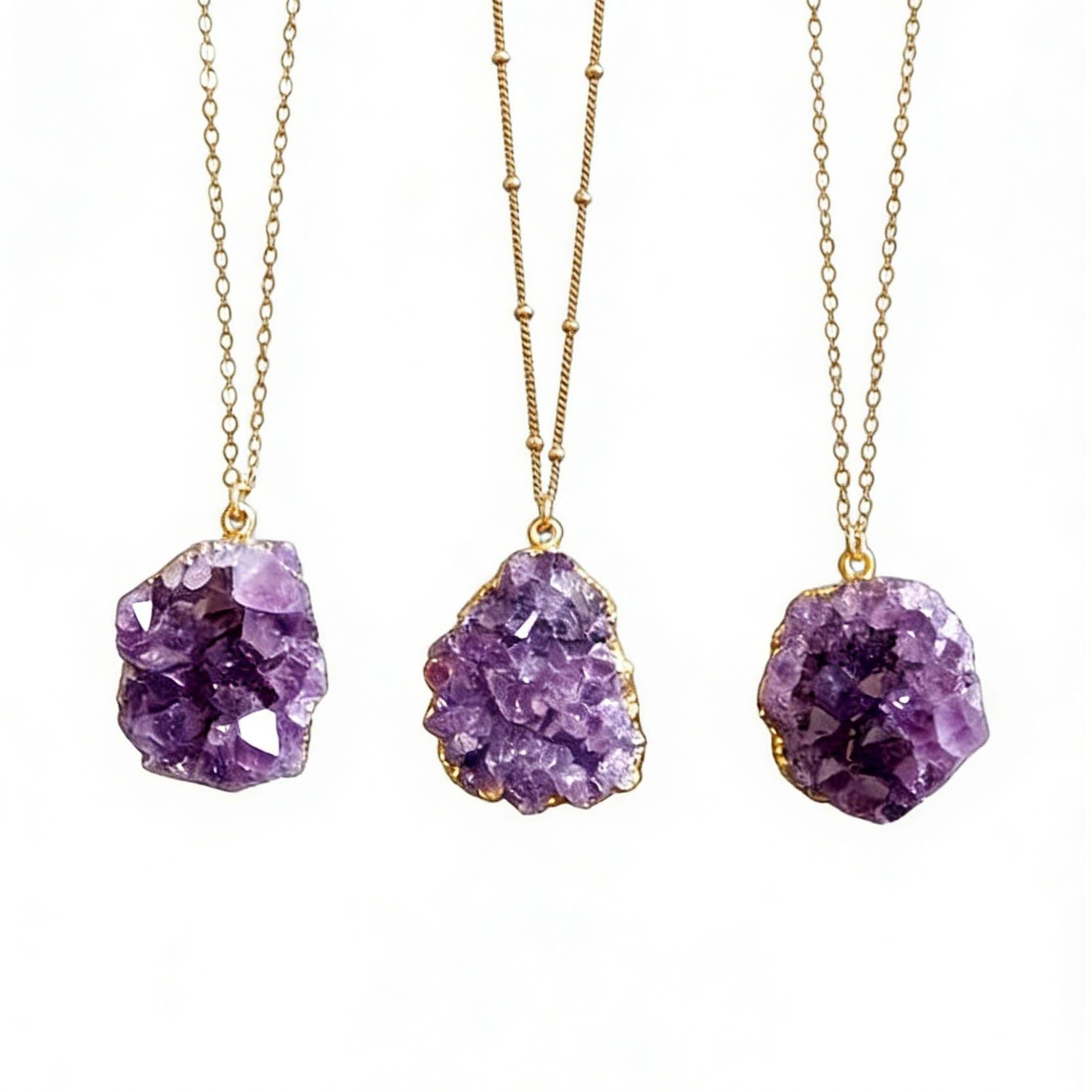 Three purple amethyst pendant necklaces on gold chains against a white background