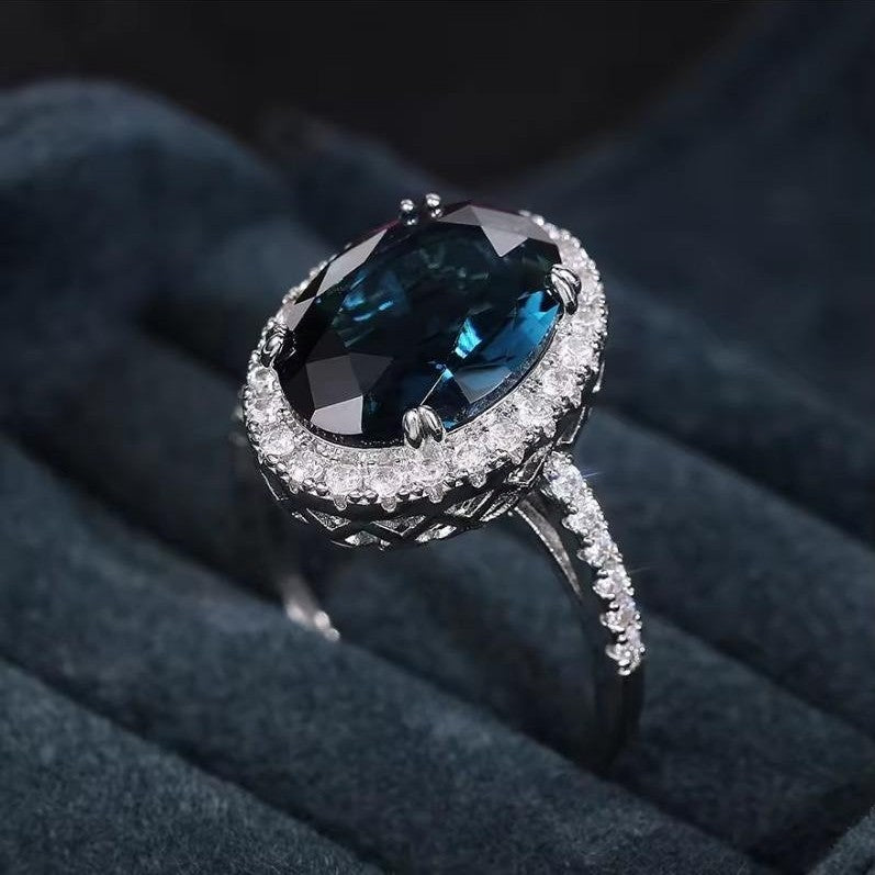 Silver ring with a large blue gemstone on a dark fabric background