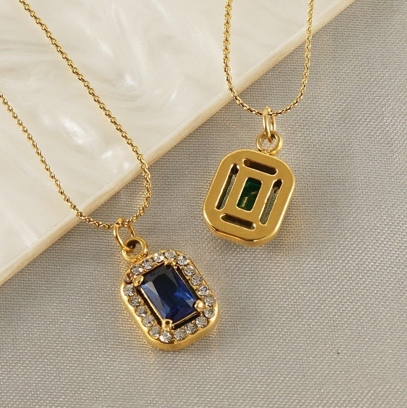 Two gold necklaces with gemstone pendants on a textured surface