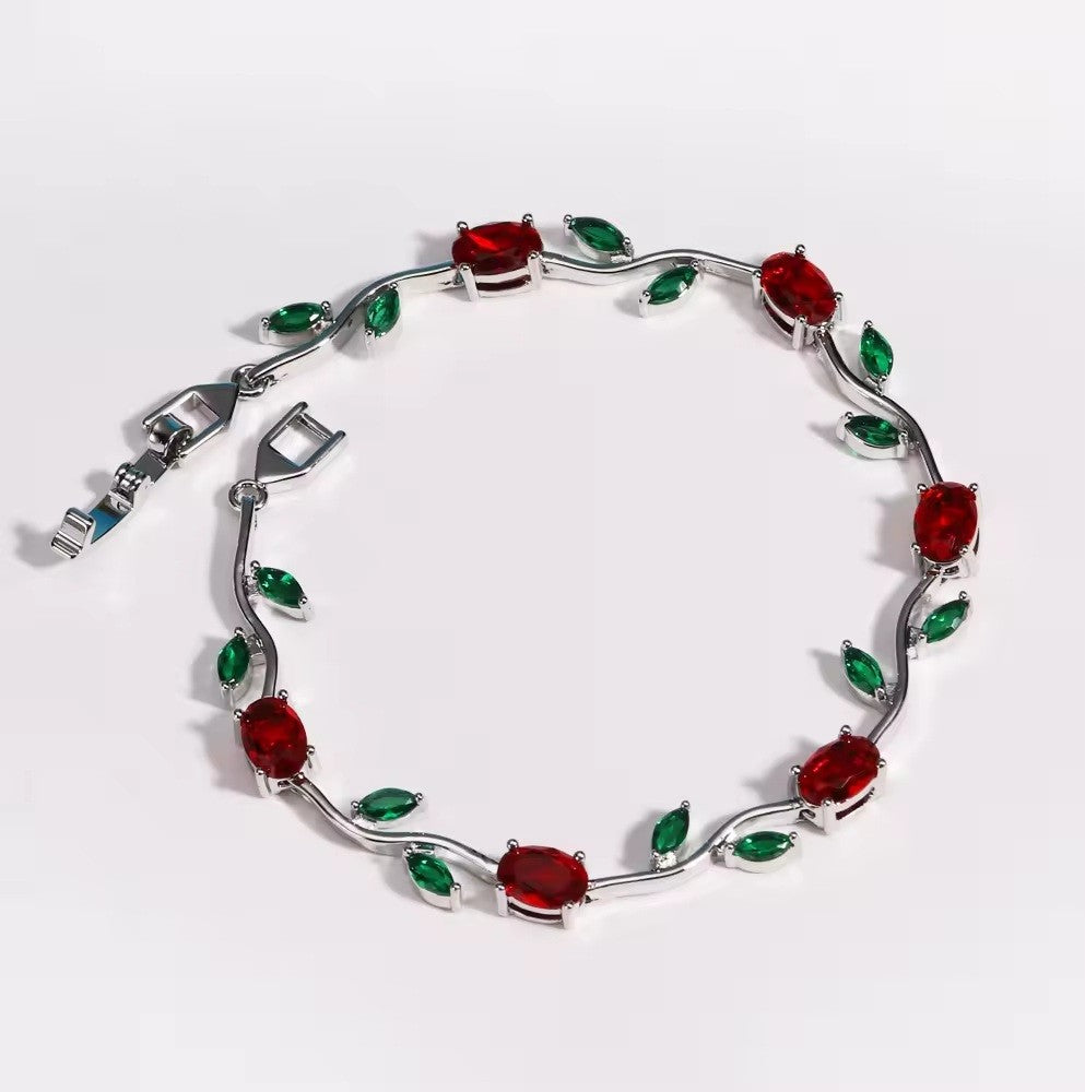 A silver vine-style bracelet featuring oval red gemstones and marquise green gemstones, displayed on a clean white background.