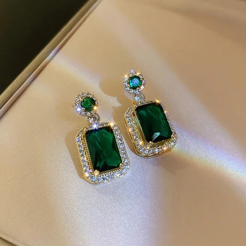 Pair of emerald green earrings with gold accents on a reflective surface.