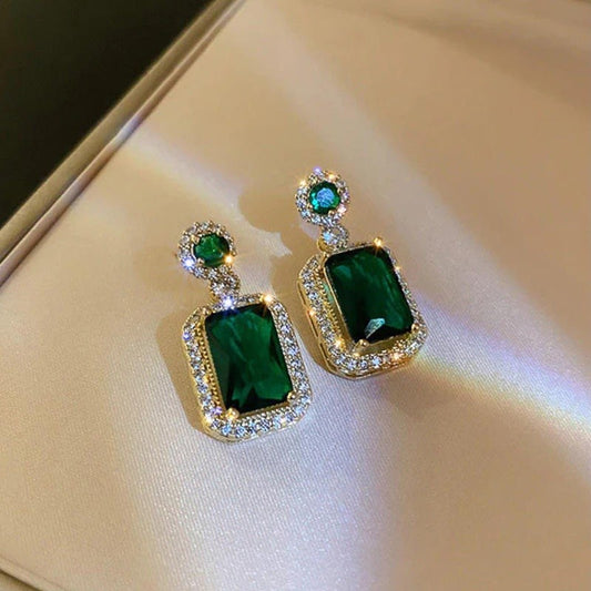 Pair of emerald green earrings with gold accents on a reflective surface.