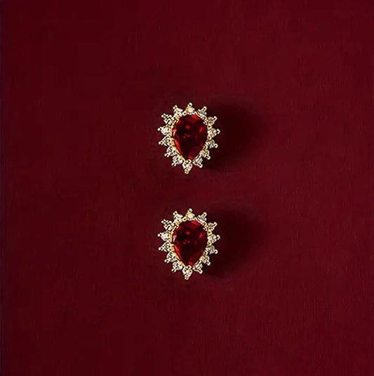 A pair of gold stud earrings featuring a central teardrop-shaped deep red gemstone 