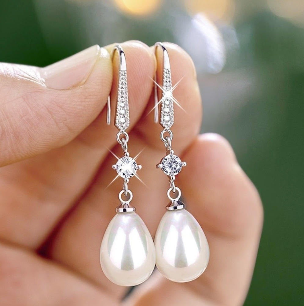 Pearl earrings with silver hooks held by a hand against a blurred green background