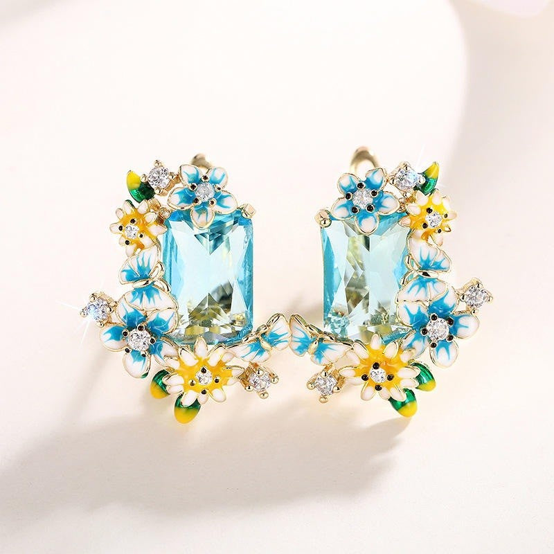 Floral-themed earrings with blue gemstones on a light background