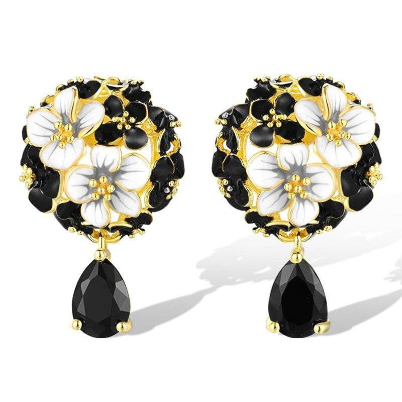 Pair of floral earrings with black and white flowers and gold accents on a white background