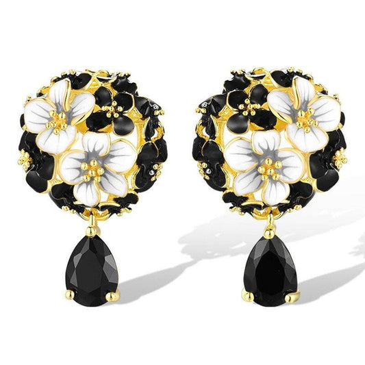 Pair of floral earrings with black and white flowers and gold accents on a white background