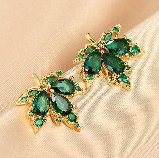 A pair of gold leaf-shaped stud earrings with green gemstones