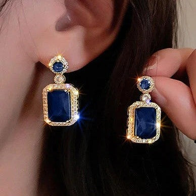 A pair of gold drop earrings featuring large rectangular dark blue gemstones