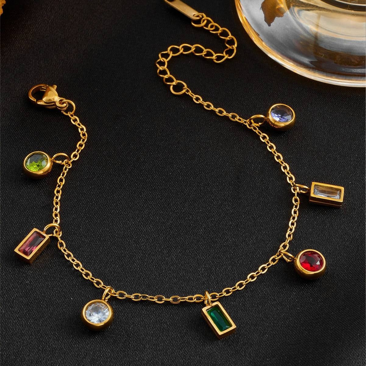 Gold bracelet with gemstone charms on a dark surface
