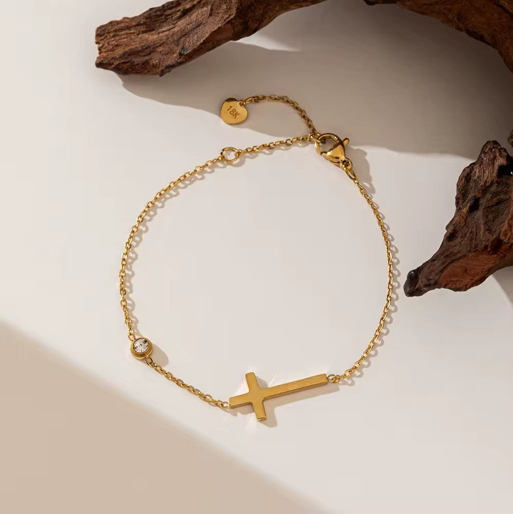 Gold bracelet with a cross charm on a neutral background