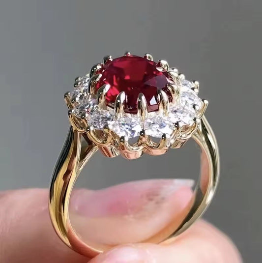 Gold ring with a red gemstone held by a hand against a gray background