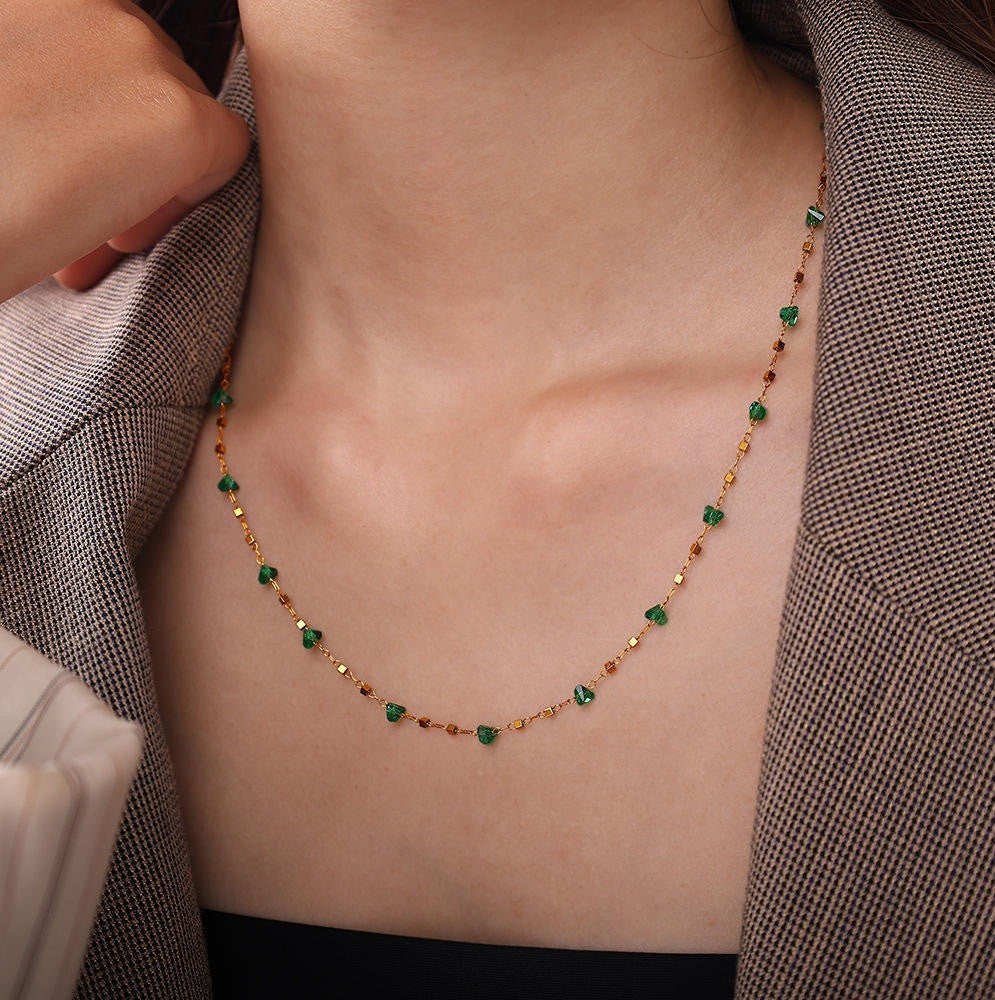 Necklace with green and gold beads on a person wearing a gray blazer.