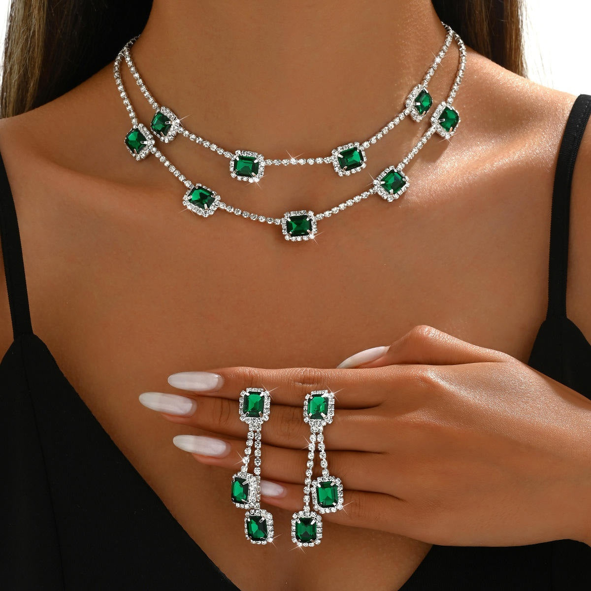 Jewelry set with emerald green stones on a model wearing a black top.
