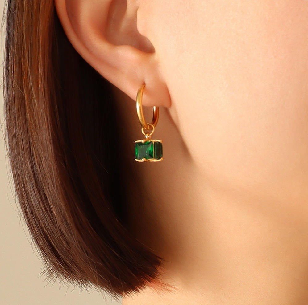Gold hoop earring with a green gemstone worn by a person.