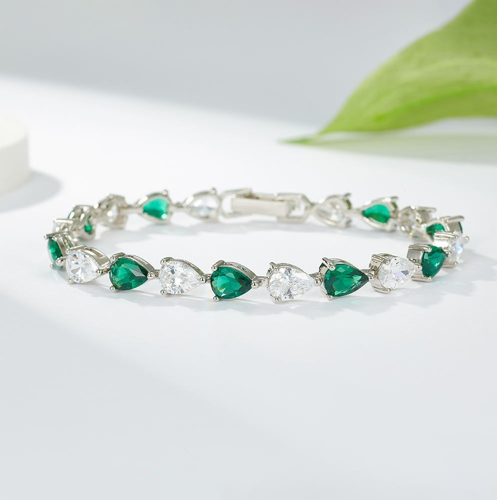 Silver bracelet with green and clear gemstones on a white background