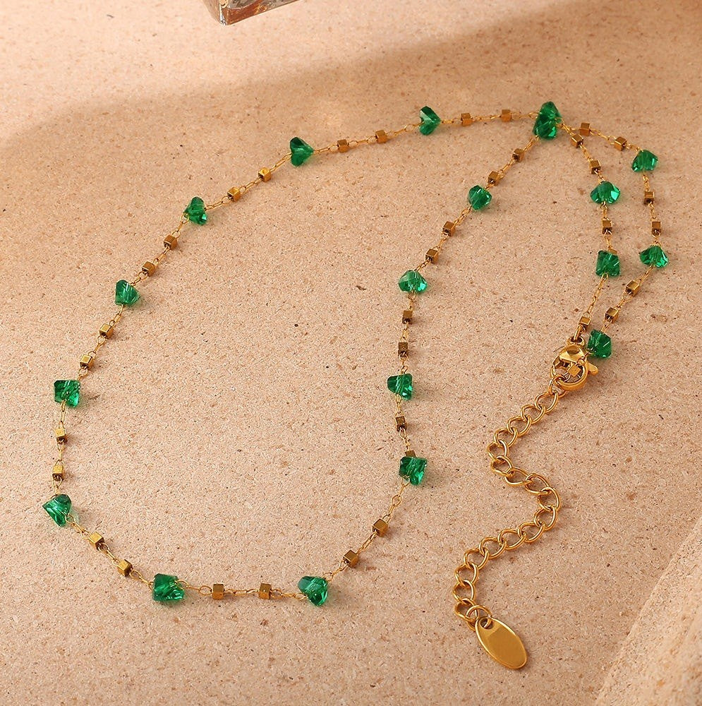 Necklace with green gemstones and gold chain on a beige background
