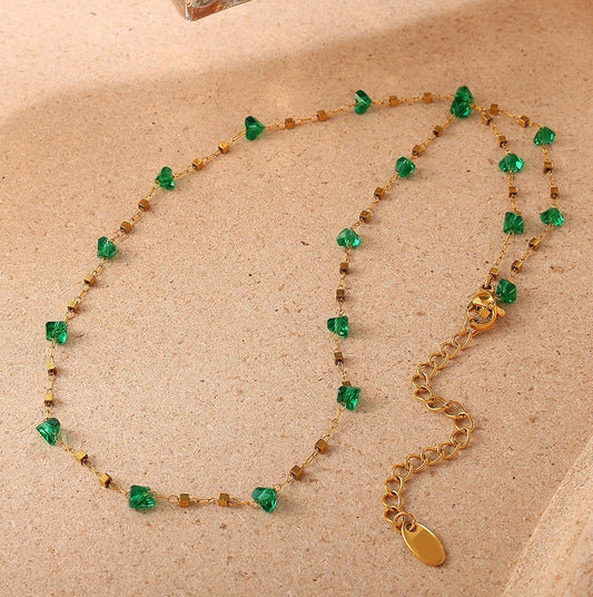 Necklace with green gemstones and gold chain on a beige background