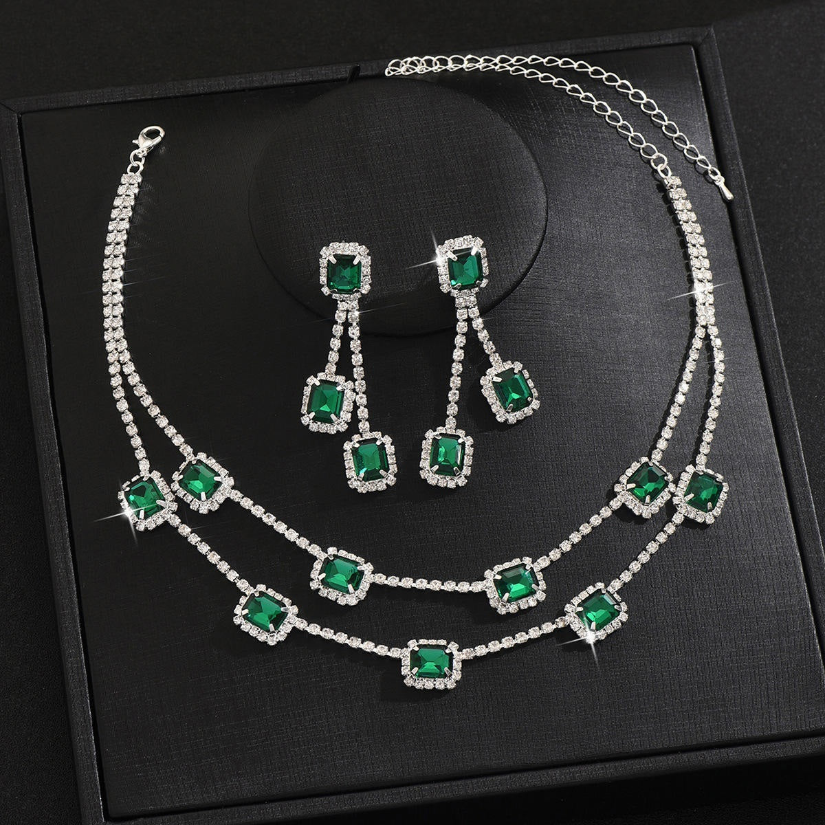 Jewelry set with necklace and earrings featuring green gemstones on a black background