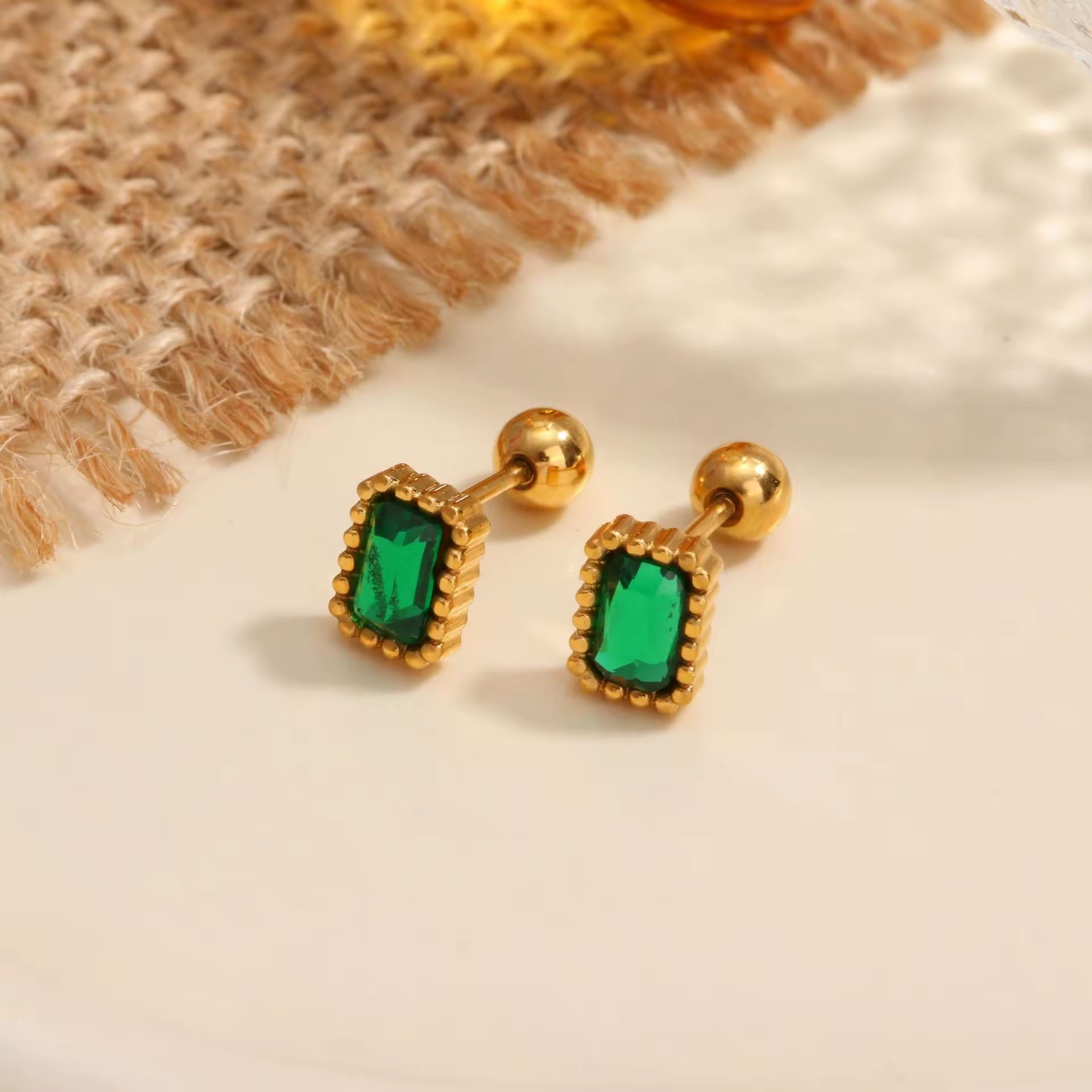 Gold earrings with green gemstones on a textured surface