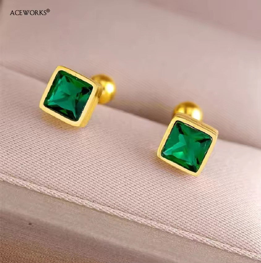Gold earrings with green gemstones on a soft fabric background