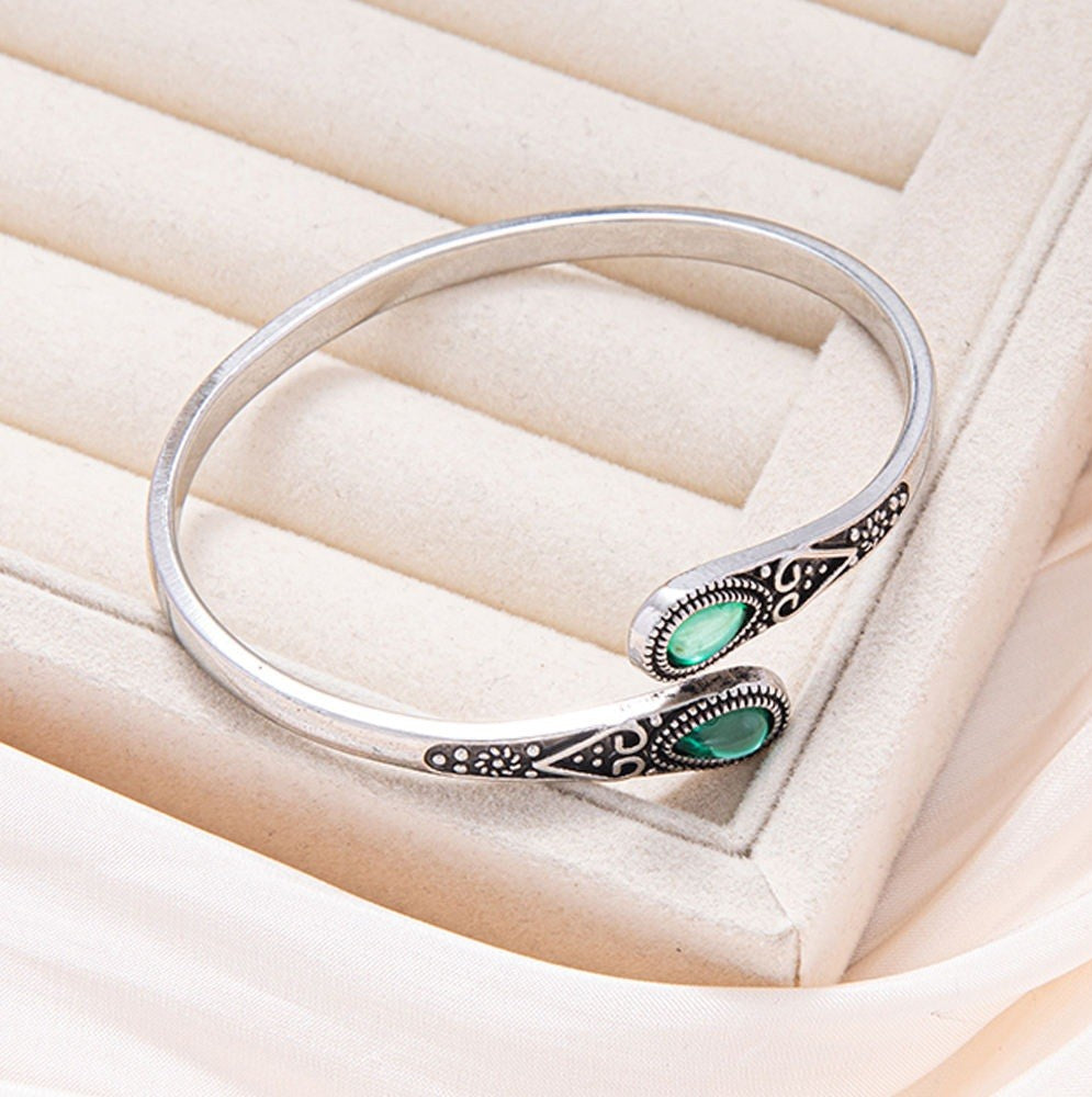 Silver bracelet with green gemstones on a soft beige background