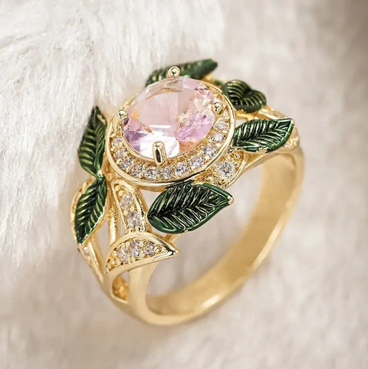 Gold ring with pink gemstone and green leaves on a white background