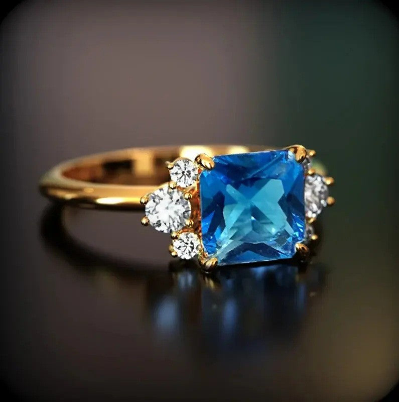 Gold ring with a blue gemstone and smaller diamonds on a dark background
