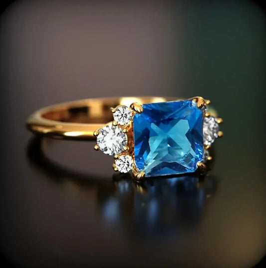 Gold ring with a blue gemstone and smaller diamonds on a dark background