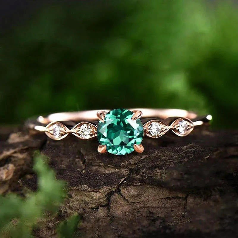 Rose gold ring with a green gemstone on a wooden surface with a blurred green background