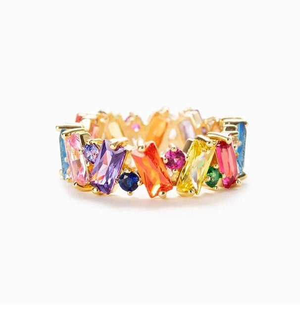 A gold-plated eternity ring featuring a continuous row of colorful baguette and round gemstones in shades of pink, purple, blue, orange, yellow, and green, set against a plain white background.
