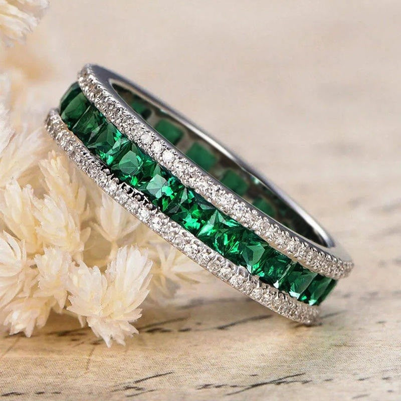 Two green gemstone rings on a textured surface with a floral background