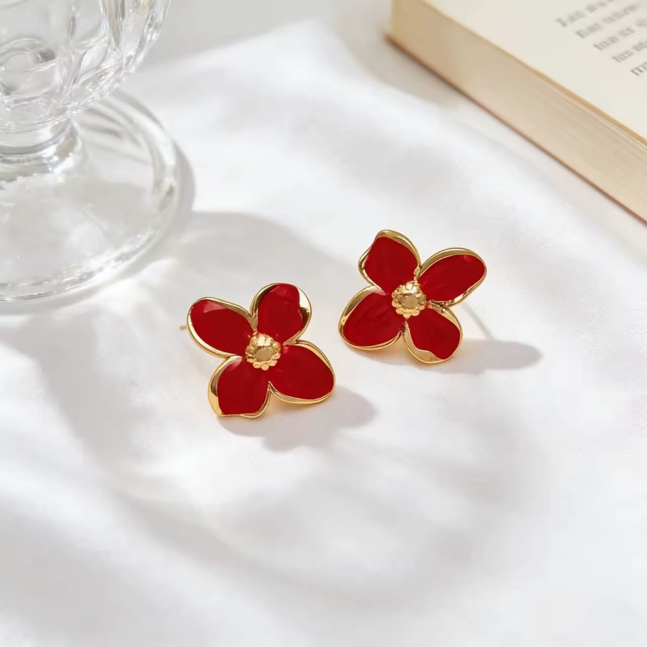 Red flower-shaped earrings with gold accents on a white surface.