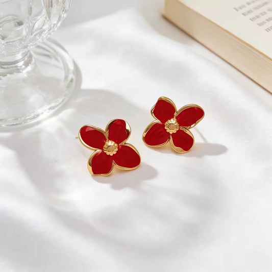 Red flower-shaped earrings with gold accents on a white surface.
