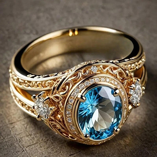 An ornate gold ring featuring a large oval blue gemstone in a detailed filigree setting with small clear accent stones, photographed on a textured dark surface.