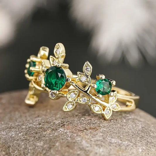 Gold ring with green gemstones on a stone surface